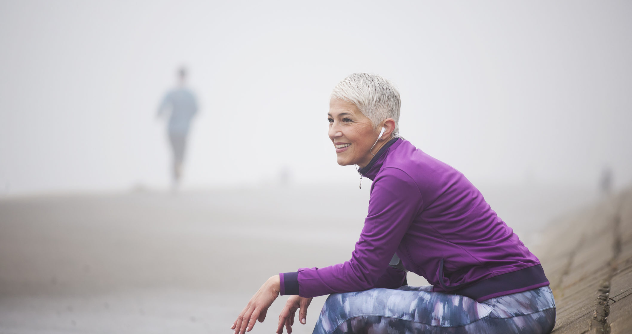 Beautiful mature woman jogging through fog in early autumn day